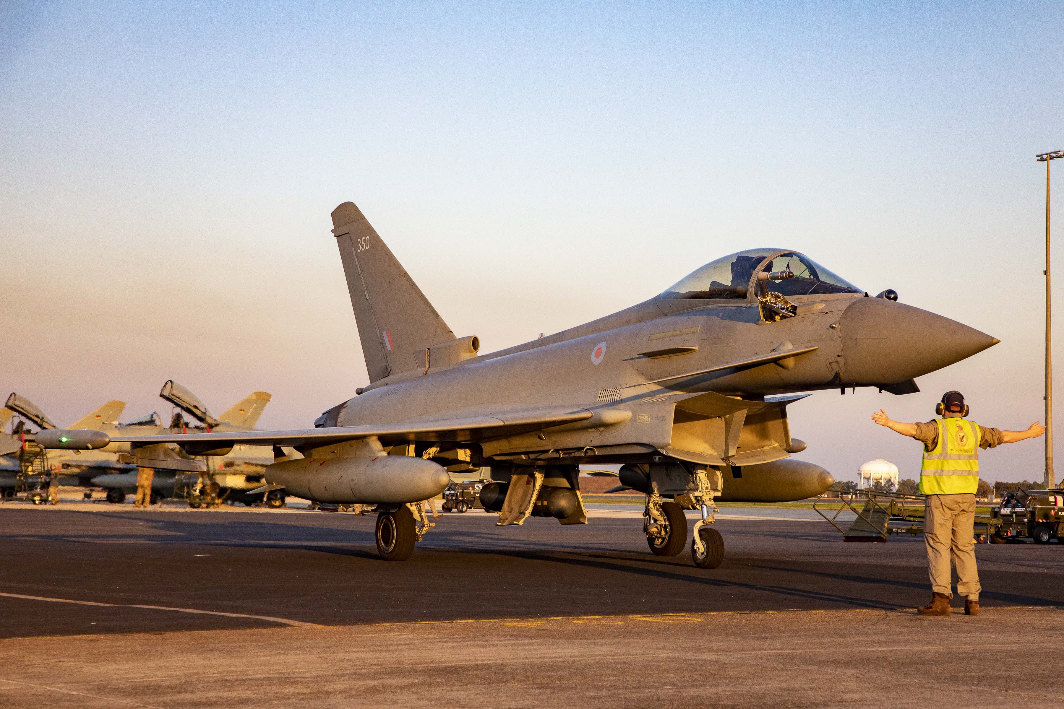 Image shows Typhoon aircraft on the airfield with RAF aviator guiding it.